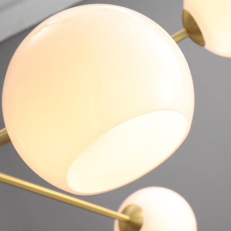 Close view of a white opal globe lit from within on this Clérachic chandelier, with a gold arm crossing the frame.
