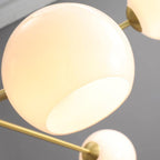 Close view of a white opal globe lit from within on this Clérachic chandelier, with a gold arm crossing the frame.