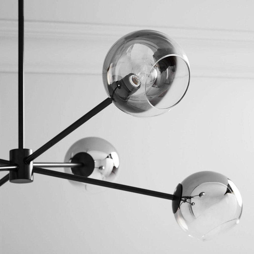 Close view of smoked glass globes on the black arms of this Clérachic chandelier, with a bulb visible in the top one.