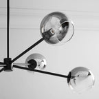 Close view of smoked glass globes on the black arms of this Clérachic chandelier, with a bulb visible in the top one.