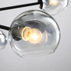 Close view of a smoked-edge clear glass globe on this Clérachic chandelier, with a warm filament bulb glowing inside.