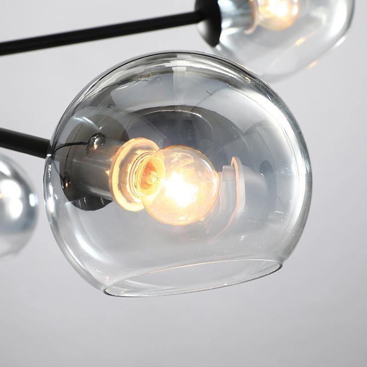 Close view of a smoked-edge clear glass globe on this Clérachic chandelier, with a warm filament bulb glowing inside.