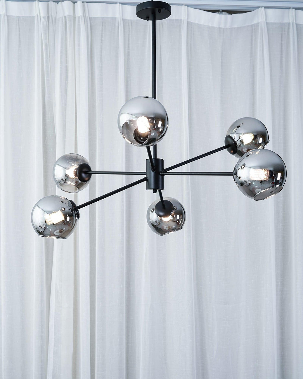 Black six-light chandelier from Clérachic with mirrored smoked globes, hung in front of floor-length white curtains.