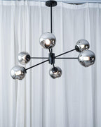 Black six-light chandelier from Clérachic with mirrored smoked globes, hung in front of floor-length white curtains.