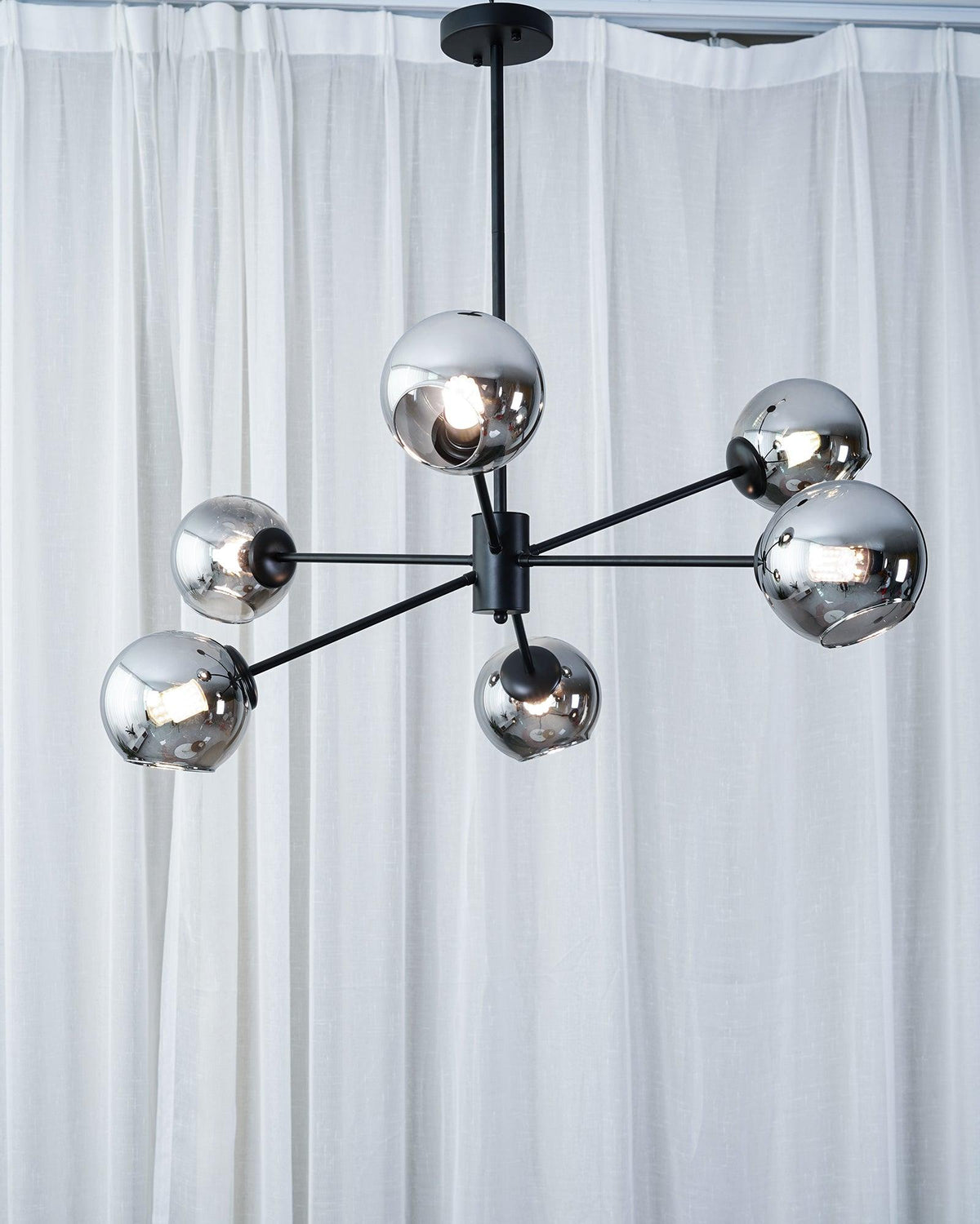 Black six-light chandelier from Clérachic with mirrored smoked globes, hung in front of floor-length white curtains.