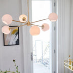 Gold Clérachic chandelier with pink-lit white globes beside an open balcony door, with a colourful framed print and a bar cart.