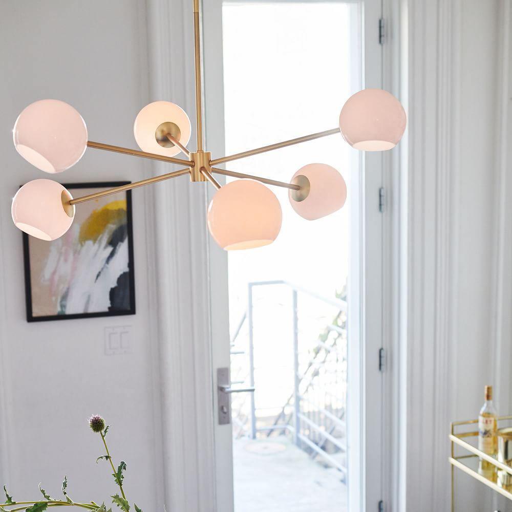 Gold Clérachic chandelier with pink-lit white globes beside an open balcony door, with a colourful framed print and a bar cart.