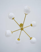Gold Clérachic chandelier seen from directly below, with six white globes on arms spreading out from a central hub.