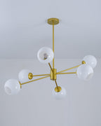 Gold chandelier from Clérachic with white globes and open-sided shades, hung from a slim rod below a plain ceiling.