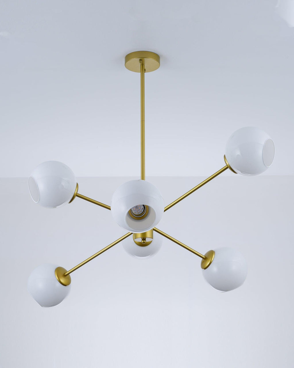Gold six-globe Clérachic chandelier with white shades, seen from below, with a bulb visible inside the centre one.