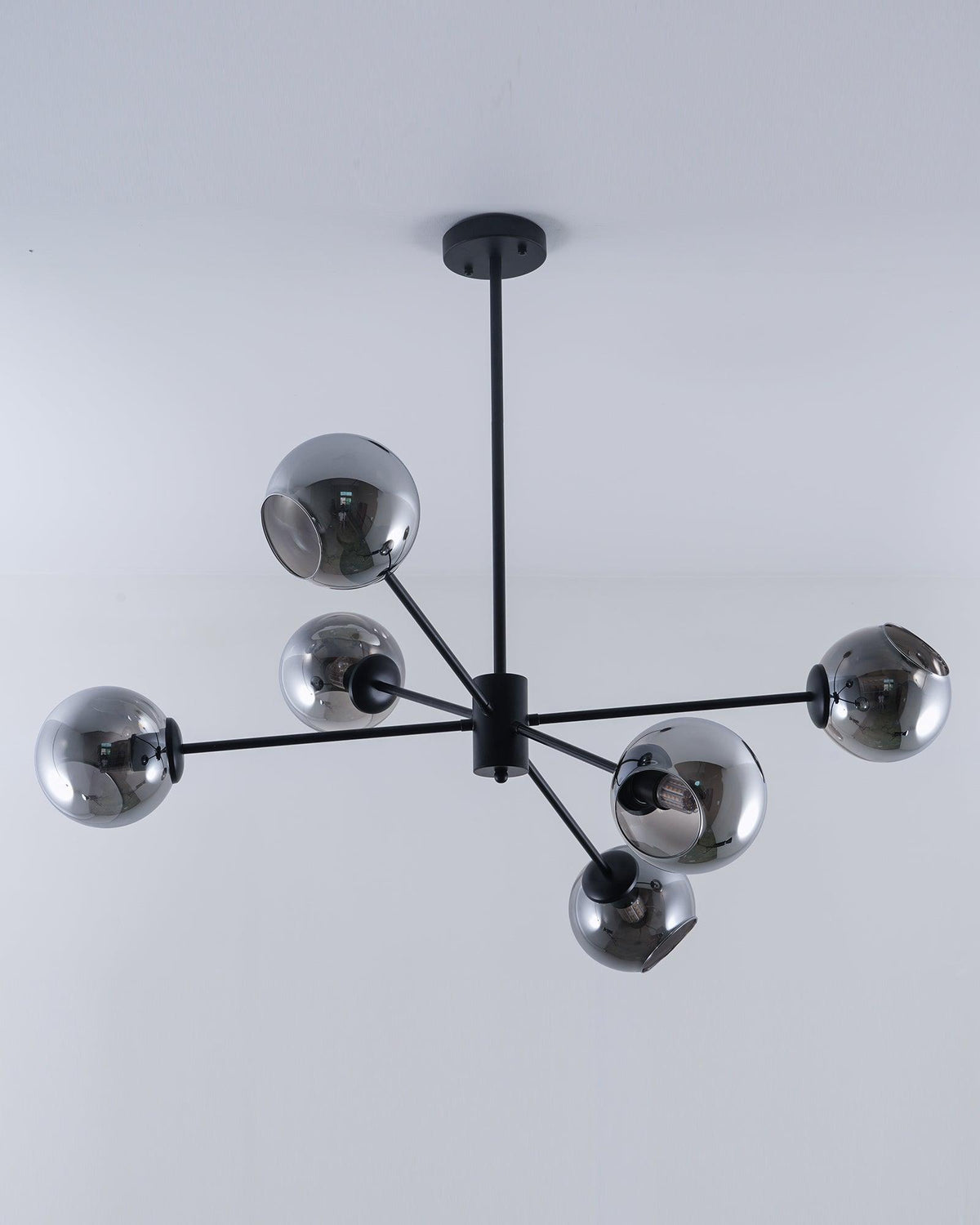 Black six-light chandelier from Clérachic with smoked glass globes, unlit, on a slim black rod below a pale ceiling.