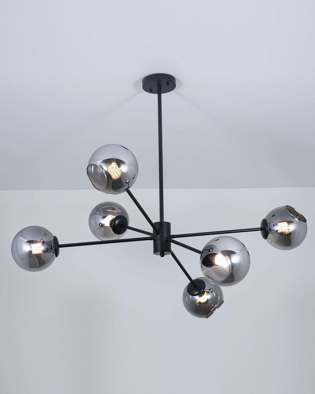 Lit black chandelier from Clérachic with smoked glass globes, each bulb glowing through the grey tint below a pale ceiling.