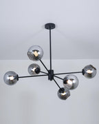 Lit black chandelier from Clérachic with smoked glass globes, each bulb glowing through the grey tint below a pale ceiling.