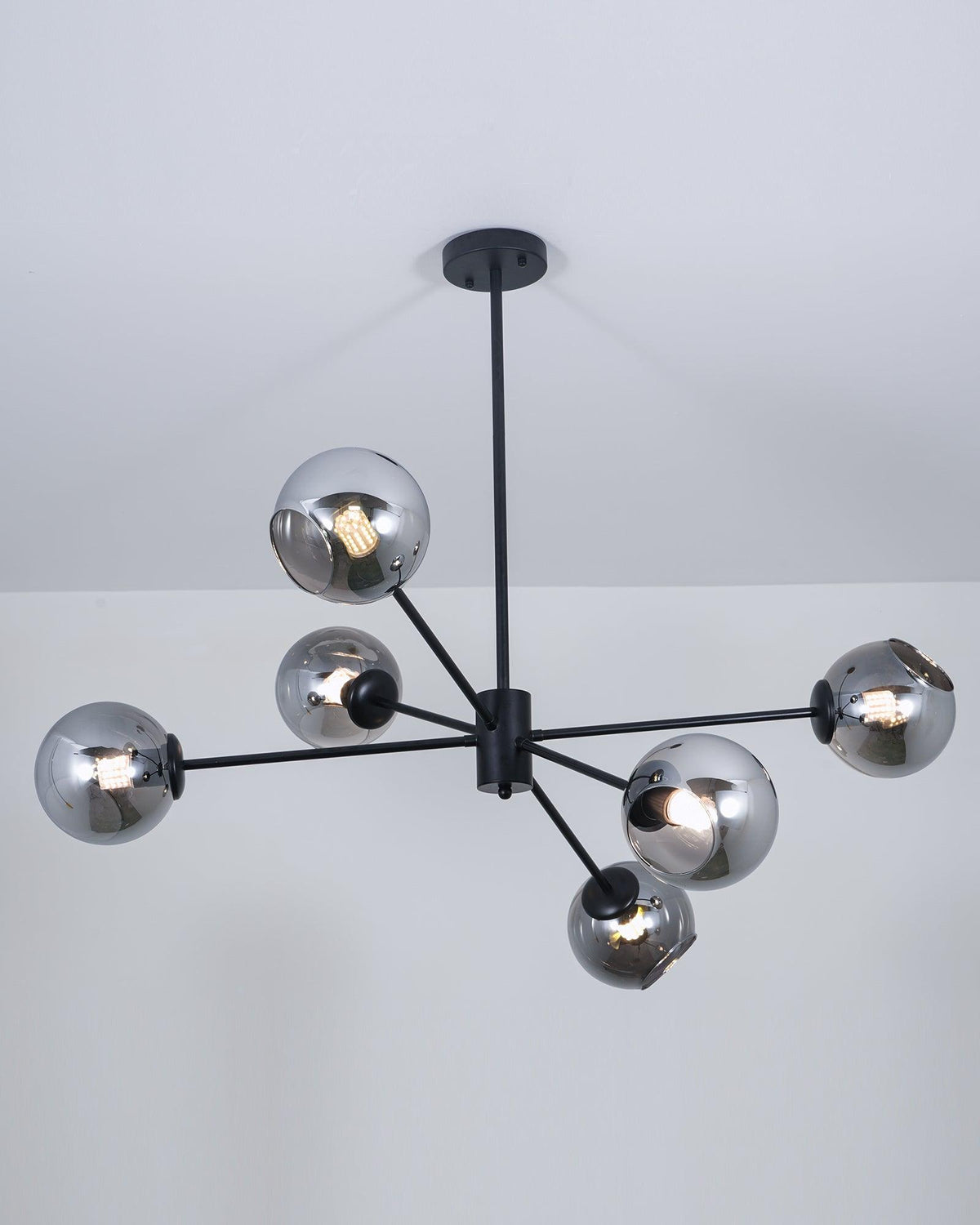 Lit black chandelier from Clérachic with smoked glass globes, each bulb glowing through the grey tint below a pale ceiling.