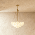 Clérachic cluster chandelier with frosted white glass spheres hanging from fine gold-toned rods, lit warmly against limewash.