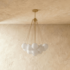 Clérachic cluster chandelier with frosted white glass spheres on slim gold-toned rods and a round canopy, shown unlit.