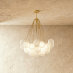 Clérachic larger cluster chandelier with many frosted glass spheres on gold-toned rods and a round gold canopy, lit.