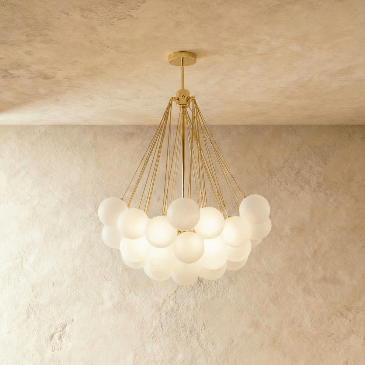 Clérachic larger cluster chandelier with many frosted glass spheres on gold-toned rods and a round gold canopy, lit.