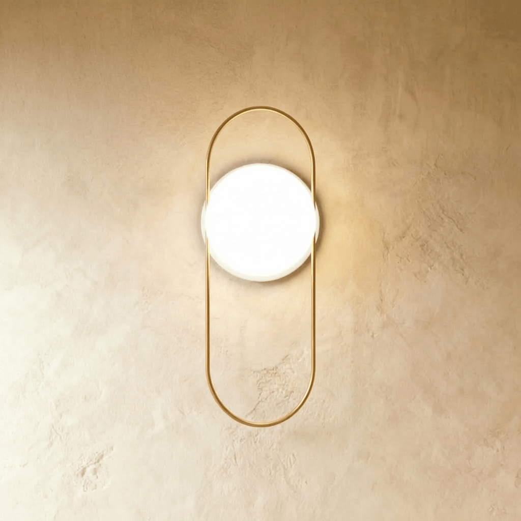Clérachic wall lamp with a tall gold loop and a round white backplate, the lit glass sphere sitting high inside the loop.