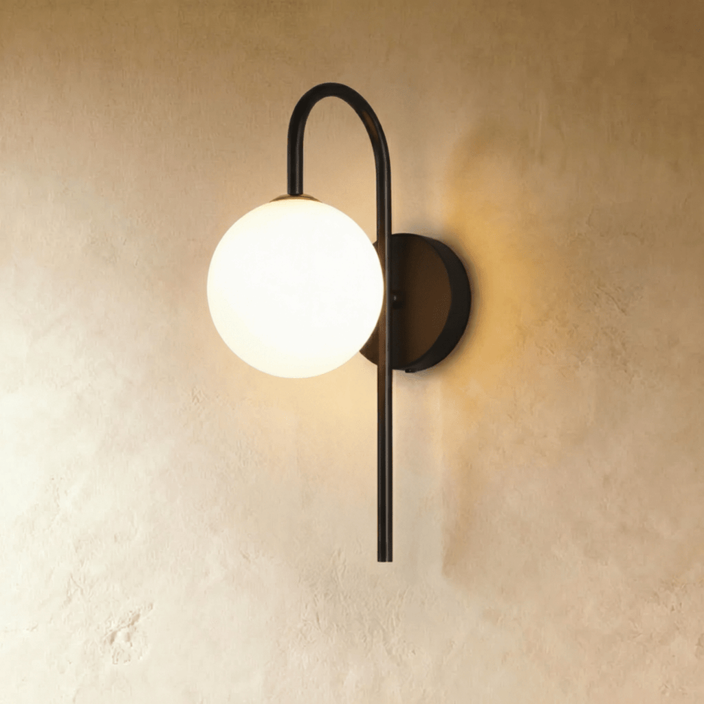 Clérachic wall lamp in black, a hooked arm curving out from a round wall plate to carry the lit sphere clear to one side.