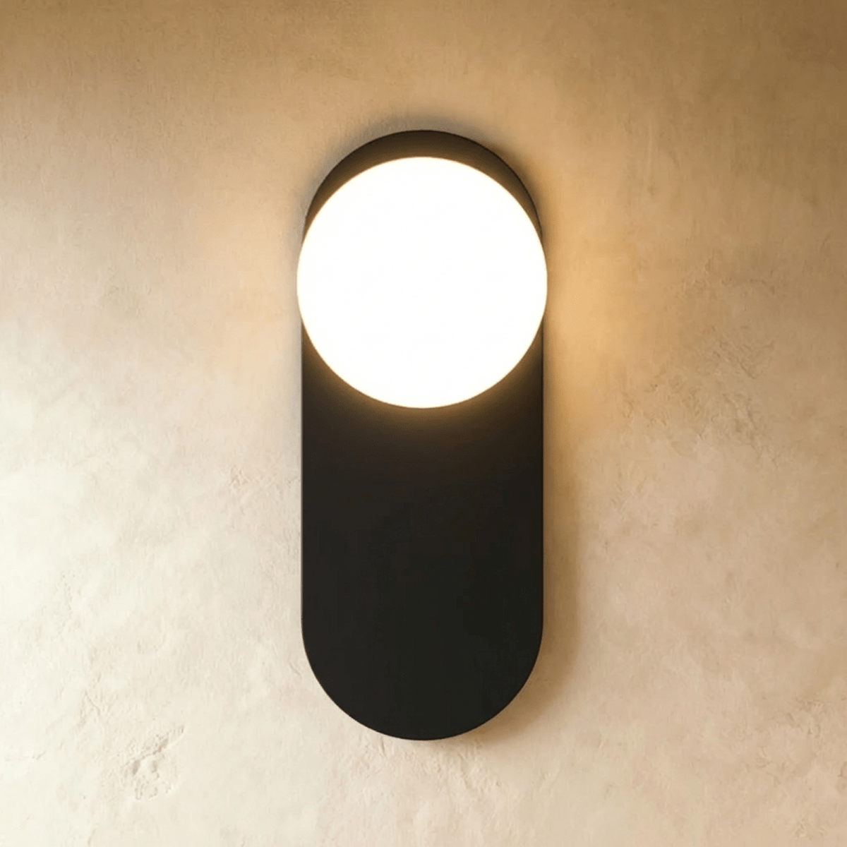 Clérachic wall lamp in black, a flat capsule-shaped plate with the lit sphere breaking out of its top edge and light spilling above and below.