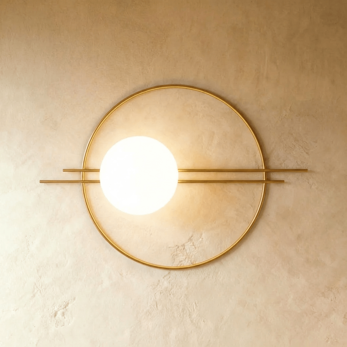 Clérachic wall lamp in gold, the wide ring and paired rods with the lit sphere placed about a third of the way in from the left.