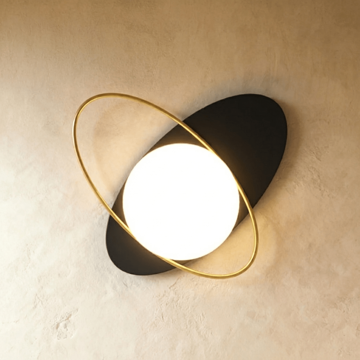 Clérachic wall lamp with a black elliptical disc tilted flat on the wall, threaded through by a gold ring around the lit sphere.