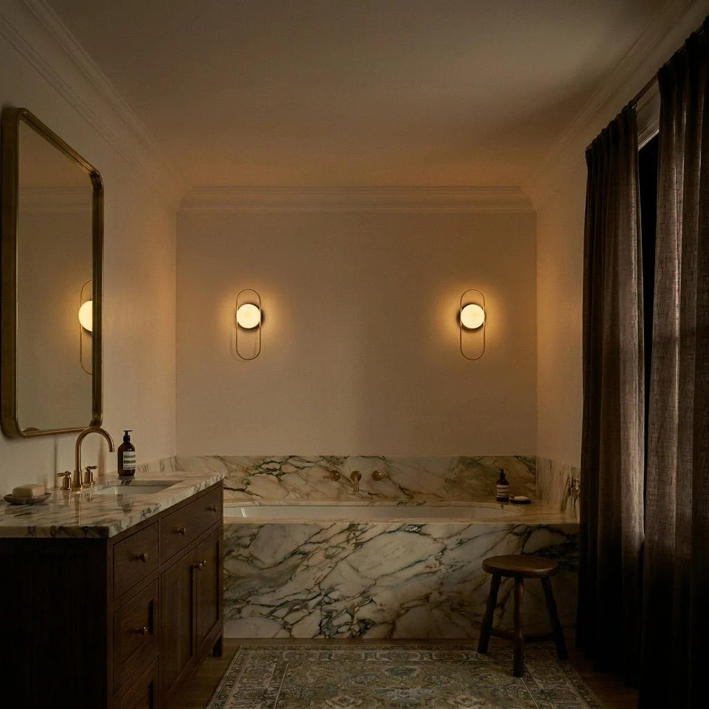 Clérachic the wall lamps in gold, the pair above the bath glowing warm as the bathroom falls into evening light.