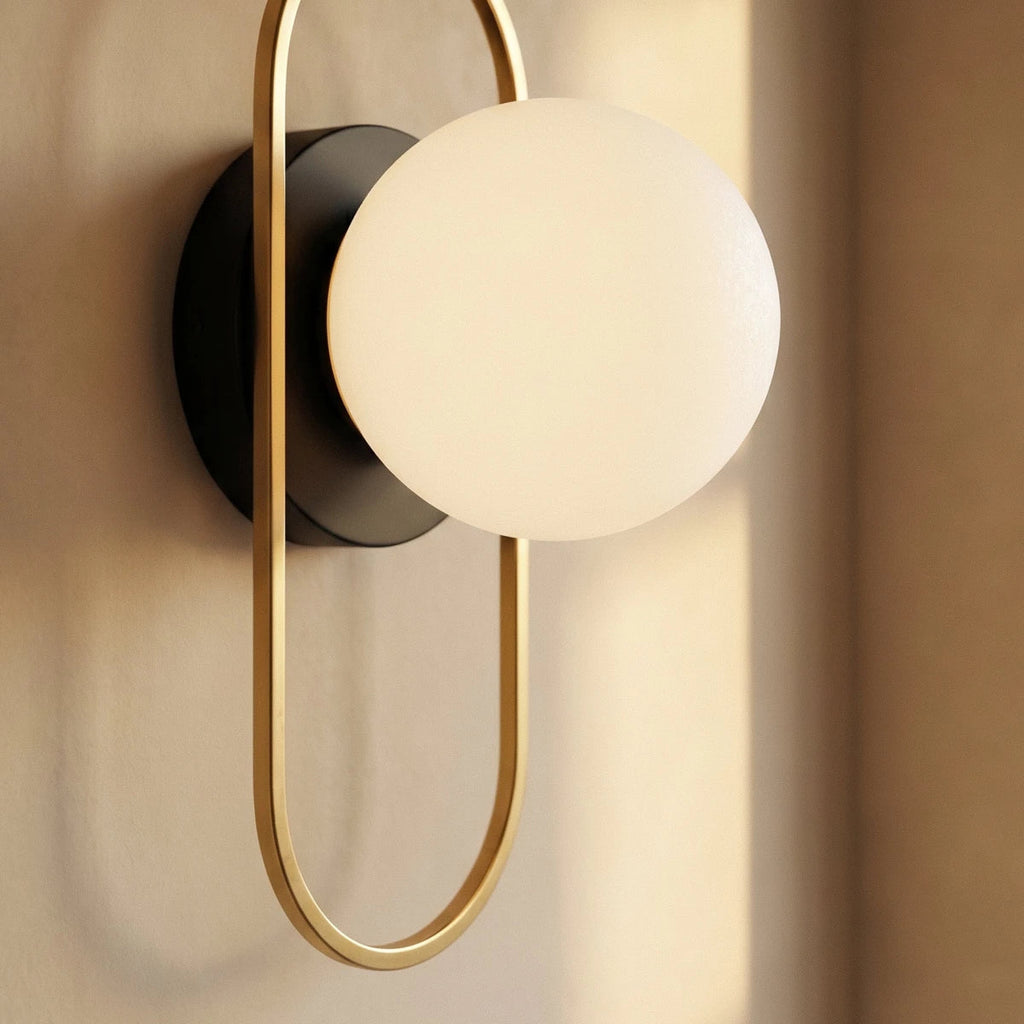 Clérachic wall lamp detail, the gold loop standing proud of its round black wall plate with the frosted glass sphere resting at the top of the loop.