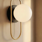 Clérachic wall lamp detail, the gold loop standing proud of its round black wall plate with the frosted glass sphere resting at the top of the loop.