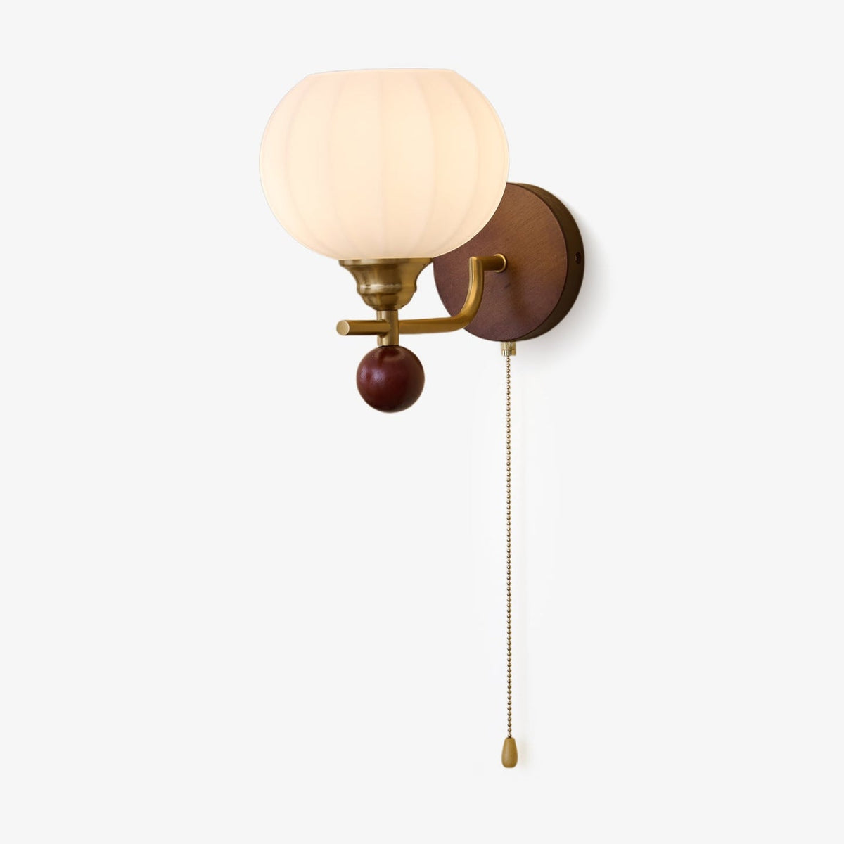 This Clérachic wall light has a ribbed frosted glass globe, a gold arm, a walnut-toned backplate and ball, and a pull chain, on white.