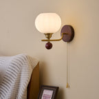 Lit Clérachic wall light with a ribbed frosted globe above a bedside, with a knitted white throw and a framed print below.