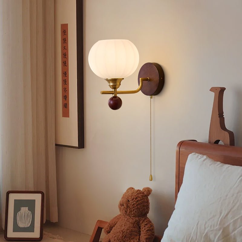 A Clérachic wall light glows softly beside a framed calligraphy print, with a teddy bear and a pillow at the bed's headboard.