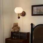 Ribbed glass Clérachic wall light lit warm above a dark wood bedside cabinet, with a teddy bear on top and a framed picture to the side.