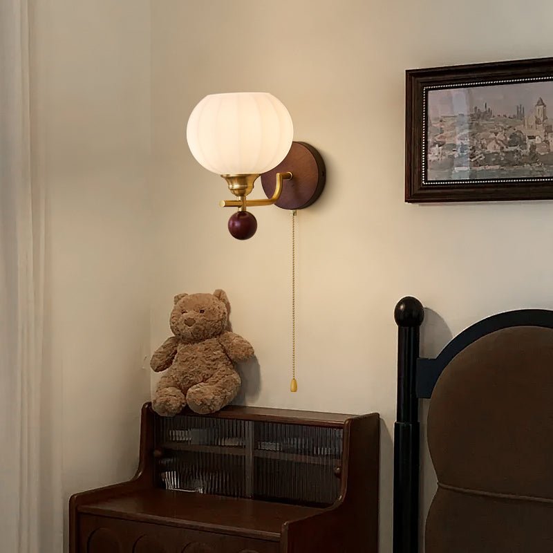 Ribbed glass Clérachic wall light lit warm above a dark wood bedside cabinet, with a teddy bear on top and a framed picture to the side.