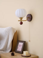 Unlit ribbed white glass globe of this Clérachic wall light, above a bedside table with a framed print and a sculpted candle.