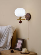 Clérachic wall light with a bright white ribbed globe, seen in daylight above a bedside table with a framed print and pine cone.