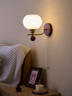 Ribbed globe Clérachic wall light glowing warm against a dusky taupe wall, above a bedside table with a framed print.