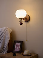 Ribbed Clérachic wall light shining brightly in a darker room, with a glow around the globe and a bedside table below.