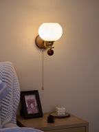 Clérachic wall light with the pull chain hanging to the left of the gold arm, above a bedside table with a framed print.