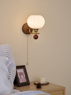 Ribbed globe wall light from Clérachic, mounted with the arm pointing left, above a bed with a white pillow and blue-edged linen.