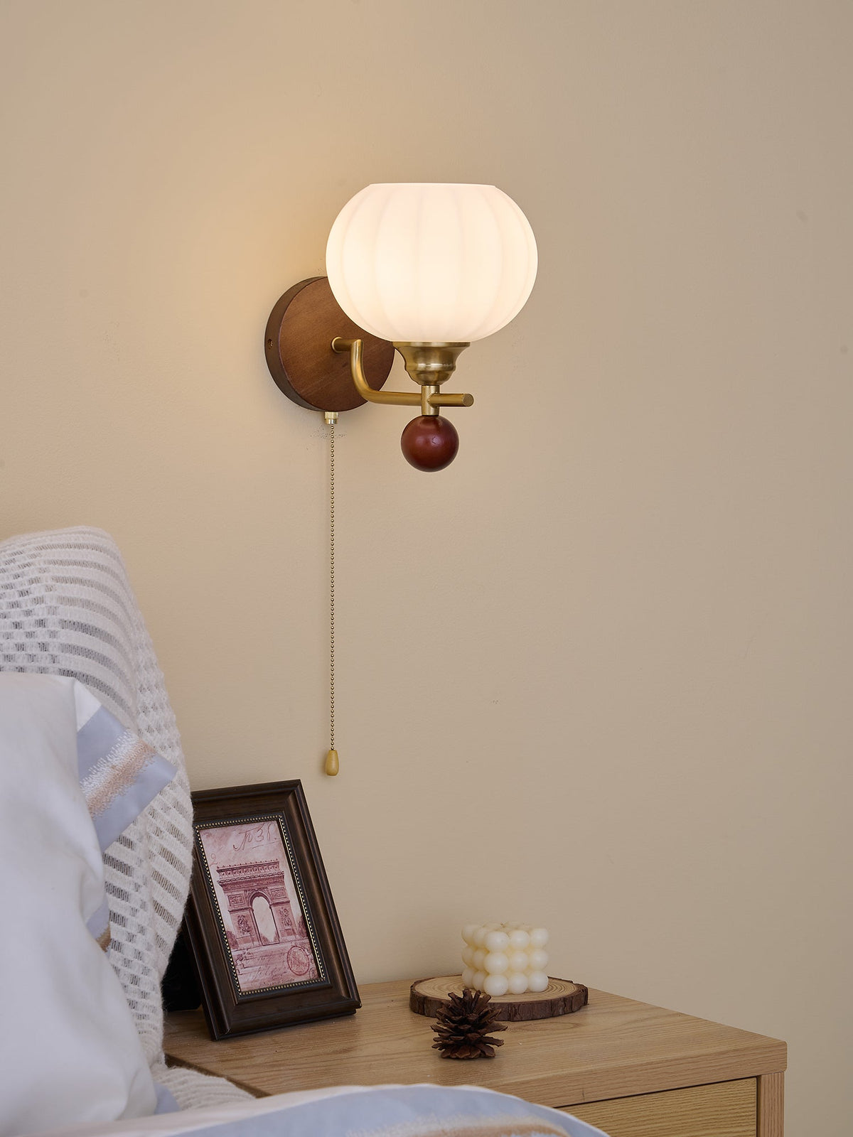 Ribbed globe wall light from Clérachic, mounted with the arm pointing left, above a bed with a white pillow and blue-edged linen.