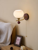 This Clérachic wall light shows the open top of its ribbed glass globe, lit warm above a bedside table with a candle and pine cone.