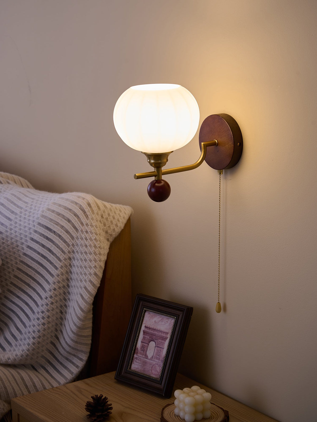 Clérachic wall light with a ribbed globe turned slightly down, in a cosy bedside corner with a framed print.