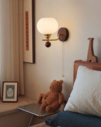Ribbed globe Clérachic wall light lit warm beside a tall framed print, a teddy bear and a pillow on a bed, with a small glass table.