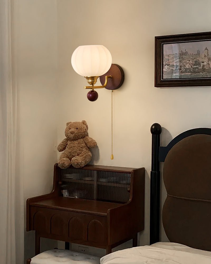 A Clérachic wall light with a ribbed globe, lit above a teddy bear on a dark wood cabinet, with a framed painting beside it.