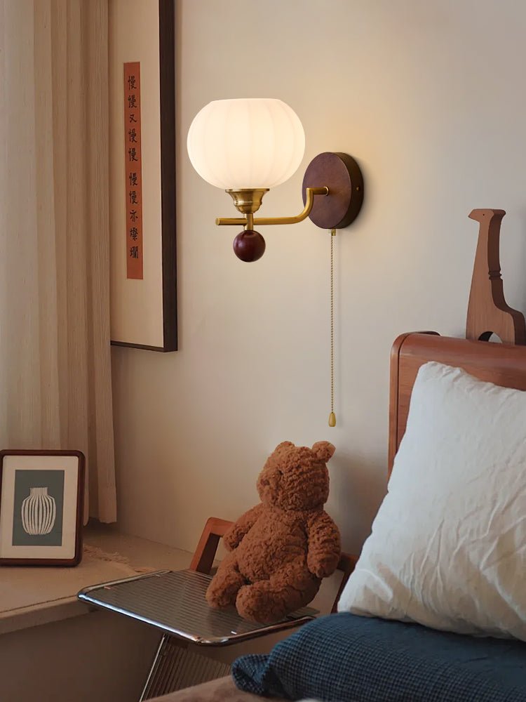 Clérachic wall light with a ribbed globe, lit warm above a glass-topped side table with a teddy bear, a pillow and blue bedding.
