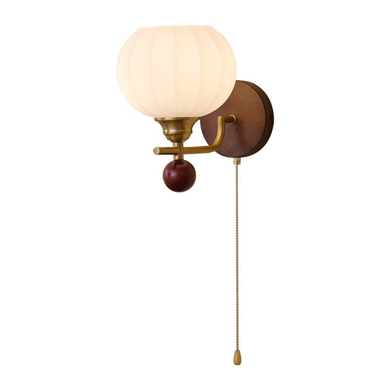 Close-up of the ribbed frosted glass globe, gold arm and walnut-toned backplate of this Clérachic wall light, with its pull chain.