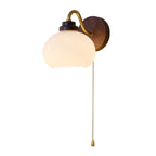 Smooth rounded glass shade, curved gold arm and walnut-toned backplate of this Clérachic wall light, shown on a white backdrop.