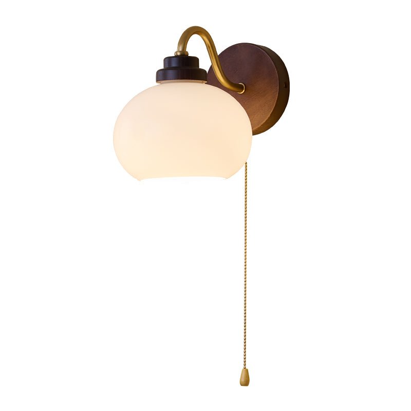 Smooth rounded glass shade, curved gold arm and walnut-toned backplate of this Clérachic wall light, shown on a white backdrop.